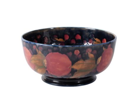 WILLIAM MOORCROFT: A "POMEGRANATE" FOOTED BOWL, painted in polychrome with fruit on a dark blue ground, signed and impressed 