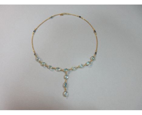 An aquamarine and sapphire necklace set in 18ct gold, set to the front with a line of nine oval cut aquamarines, all spectacl