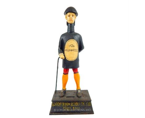 A cast iron, painted, reproduction Guinness money box in the form of a standing gentleman, legs astride and holding a walking