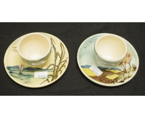 Two Martin Boyd ceramic egg cups each hand painted decoration, with attached under plates, and with inscribed mark to base, (
