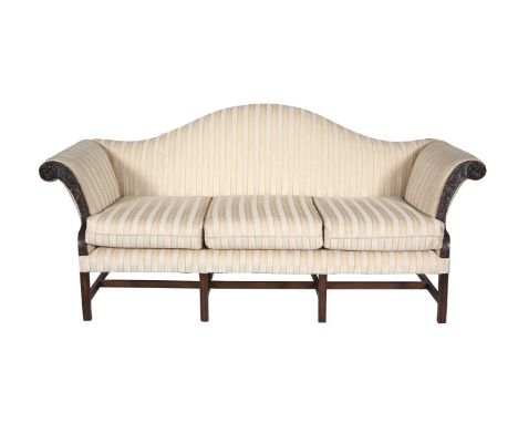 A GEORGE III MAHOGANY FRAMED FOUR SEAT CAMEL BACK SOFA, upholstered in striped cream fabric, the outscrolling arms carved wit