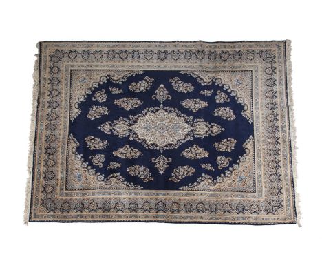 A LARGE PERSIAN WOOL RUG, the central reserve containing a dominant golden flower head motif against the deep navy ground, su