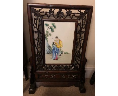 A Chinese carved hardwood firescreen with central ceramic plaque. Firescreen slides out from stand. Very good condition. 79cm