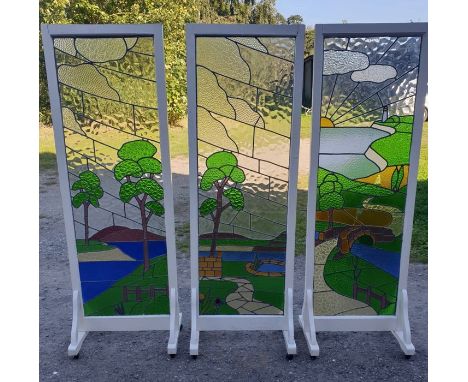 Three stained glass panels set in wooden frames on rollers, 1 panel glass slight a/f. 190 h x 63cms w. Legs 41cms d. Glass 16