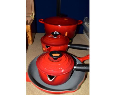 FOUR LE CREUSET ENAMEL PANS, each in red enamel over cast iron, comprising 23cm skillet pan, two saucepans with lids and pour
