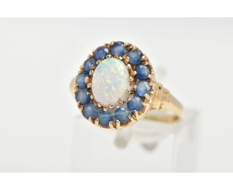 A 9CT GOLD, OPAL AND BLUE STONE RING, an oval opal approximate dimensions length 8mm x width 6mm, prong set with a halo of ci