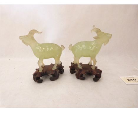 A pair of Chinese carved jade rams on hardwood bases. The figures 3¾' high. Damage and repairs