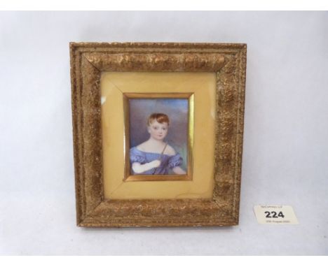 A 19th century portrait miniature of a child wearing a blue off the shoulder dress and holding a hunting crop