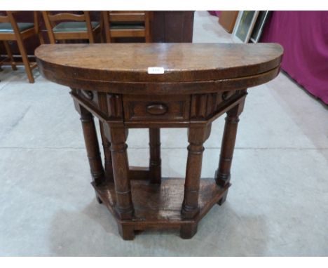 An antique semi-circular oak folding (credence) table, the panelled frieze with a drawer, raised on four plain ring turned le