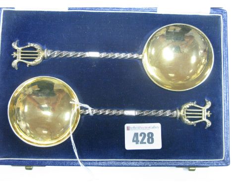A Matched Pair of Hallmarked Silver Serving Spoons, each with circular gilt bowl and twisted handles with lyre finial, in ori