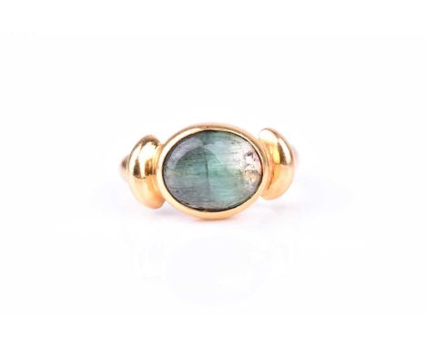 A yellow gold and cats eye tourmaline ringset east to west with an oval cabochon green tourmaline, showing chatoyancy to ston