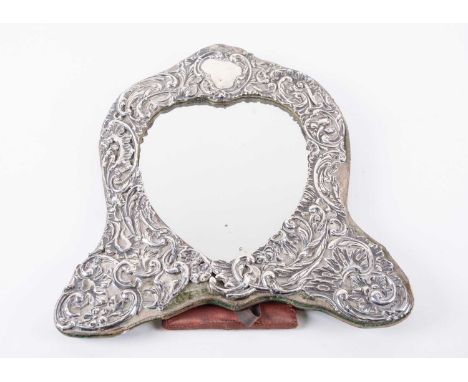 An Edwardian silver mounted dressing table mirror, Chester 1904, the heart shaped mirror framed by rococo scrolls and foliage