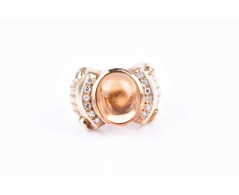 A yellow metal, diamond, and cabochon citrine ring, set with an oval cabochon stone, the stylised shoulders inset with small 