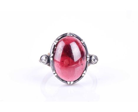 An unusual diamond and garnet ring, set with an oval cabochon garnet, set in a silver mount, flanked with two collet-set rose