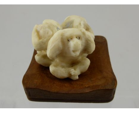 A Japanese Ivory Carved Netsuke depicting the three monkeys.  The carved figure having character mark to base on hardwood sta