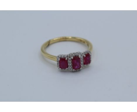 A ruby and diamond trilogy ring in 18ct yellow gold. Set with three step cut rubies, to an estimated 0.67 carats, and surroun