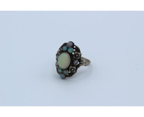 An Arts and crafts style opal set flower ring.  In precious white metal assessed as silver. Unmarked. Size N1/2. Gross weight