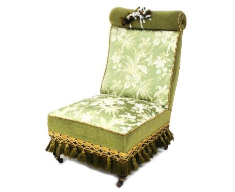 A Victorian mahogany nursing chair, upholstered in green floral fabric, with a tasselled border, on turned legs with ceramic 