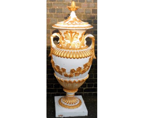 A Victorian style composition garden urn and cover, the lid with a pineapple finial, the base with two handles and cast with 