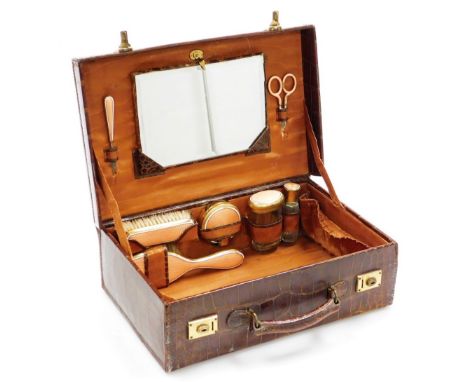 An early 20thC crocodile leather toilet case, the lid initialled A.P., containing various brass and coral coloured guilloche 