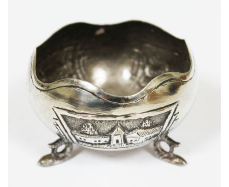 An Eastern white metal bowl having decorated panels depicting buildings and sat on three dolphin feet, marked 'Silver', diam.