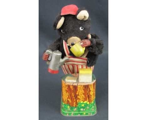 Japanese tinplate model of a bear dressed in an apron and cap, on naturalistic foliate base, drinking a cup of tea, featuring