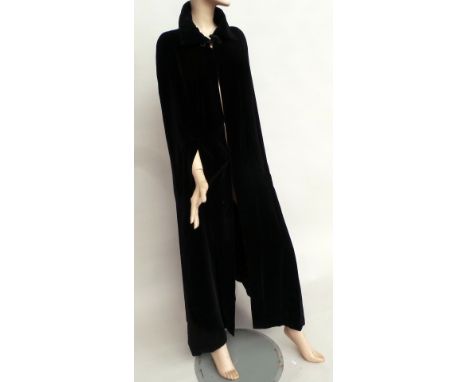A full length black velvet 1070s cloak labelled 'Quad'. Garment fastens with a toggle at the neck and has a quilted lining, t