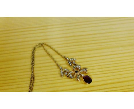 A 9 carat gold pendant of tied bow form set with seed pearls with an oval claw set garnet suspended drop, all on a 9 carat go