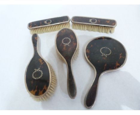 A George V silver and tortoiseshell dressing table set comprising hand mirror (plate cracked) two hair brushes and a pair of 