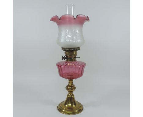 A Victorian brass oil lamp, with a cranberry glass reservoir and an etched glass shade, 59cm tall