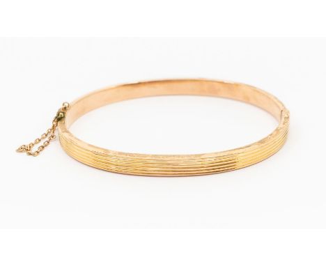 A 9ct gold hinged bangle, ridged decoration, width approx 5mm, internal diameter approx 63mm, weight approx 9.9gms Further de