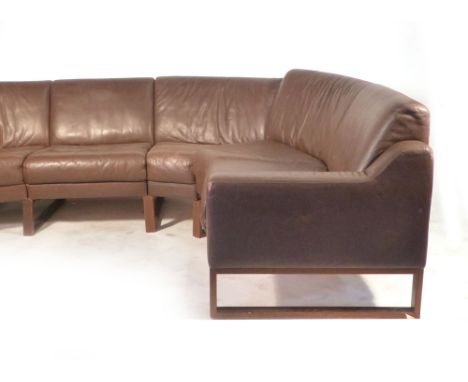 A 1970's brown leather U-shaped sofa on stained beech supports CONDITION REPORT: cracking and fading to leather in places thr