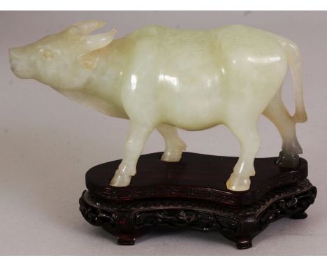 A CHINESE CELADON JADE MODEL OF A WATER BUFFALO, striding forward, together with a wood stand, the carving itself 5.75in long