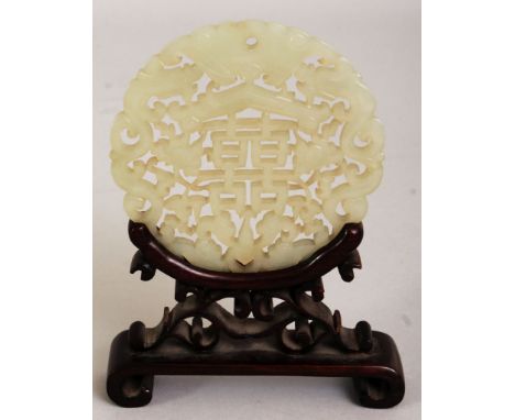 A CHINESE PIERCED CELADON JADE CIRCULAR PLAQUE, together with a fitted wood display stand, the jade pierced and carved to its