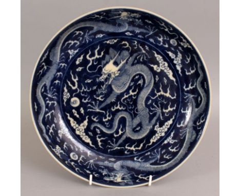 A CHINESE BLUE & WHITE PORCELAIN DRAGON DISH, of saucer shape, the decoration reserved on a blue wash ground, the base with a