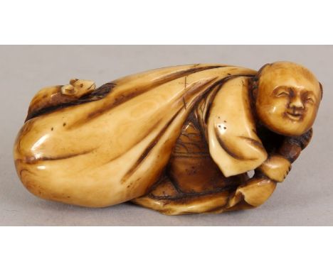 AN EARLY 20TH CENTURY SIGNED JAPANESE MEIJI PERIOD STAINED IVORY NETSUKE OF A BOY PULLING A LARGE BAG, the bag carved in reli