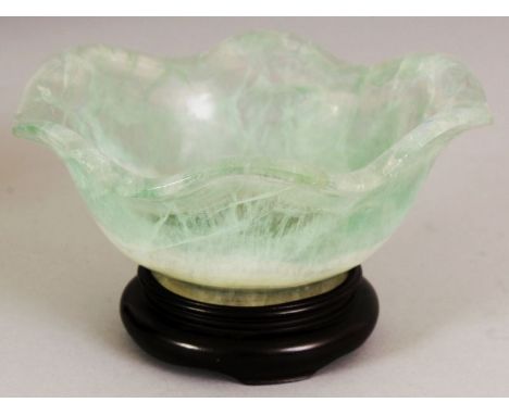 AN UNUSUAL CHINESE CRYSTAL BOWL, with a wavy rim, together with a wood stand, the transparent stone with opaque white and lig