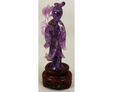 A CHINESE AMETHYST FIGURE OF GUANYIN, together with a fitted wood stand, the Goddess holding a flower spray, 5.75in high over