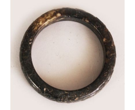 AN EARLY 20TH CENTURY CHINESE ARCHAIC STONE BANGLE, the sides carved in low relief with taotie, the predominantly black stone