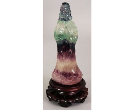 A CHINESE FLUORITE FIGURE OF GUANYIN, together with a carved wood stand, the Goddess standing in prayer, the stone of varied 