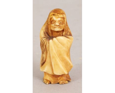 A SMALL JAPANESE MEIJI PERIOD STAINED IVORY NETSUKE OF DARUMA, standing in an enveloping hooded robe, 1.6in high.