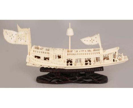 AN EARLY 20TH CENTURY CHINESE CANTON CARVED IVORY MODEL OF A RIVER BOAT, together with a fixed wood stand, 4.9in high overall