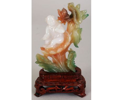 A CHINESE FLUORITE MODEL OF A SMALL BOY, seated on a lotus leaf and holding a lotus spray, 4.7in high overall, the carving it
