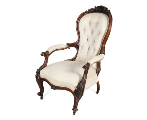 A Victorian carved walnut framed balloon back armchair. With craved leaves and scrolls, button back, with cream textured upho