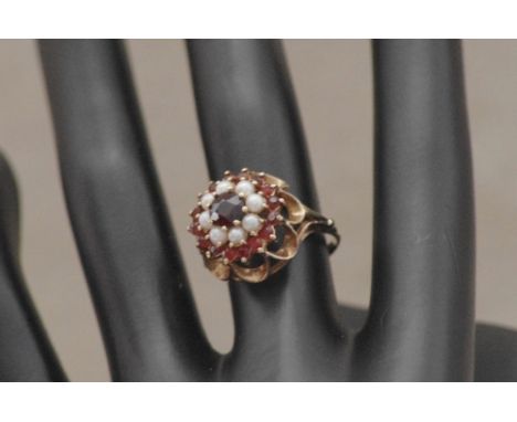 A 9ct gold, pearl and ruby dress ring set in a three tiered setting in the form of a flower, raised on a circle of eight arch