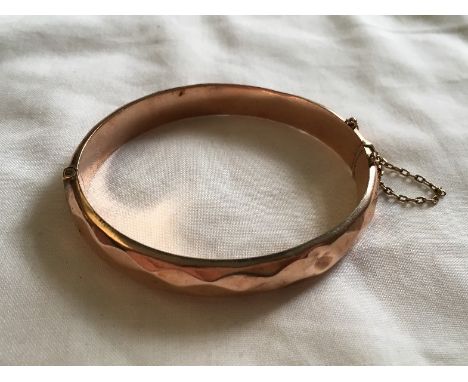 A 9ct rose gold bangle with safety chain, approximately 13 grams.
