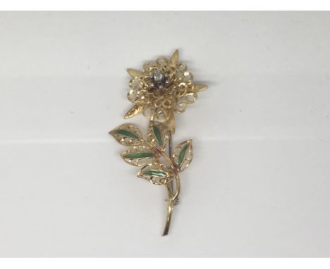 A gold flower brooch marked 750 set with small diamonds  and green enamel leaves