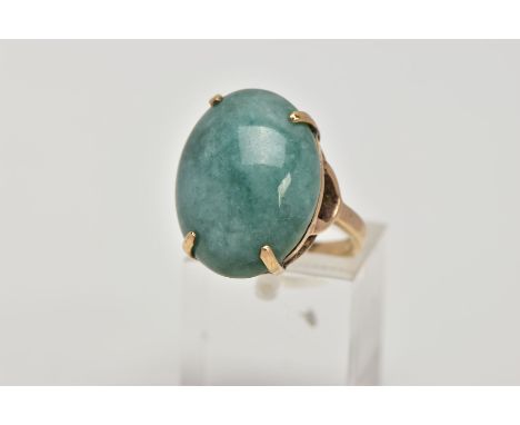 A YELLOW METAL DRESS RING, designed with a claw set, oval green stone assessed as jade, openwork gallery leading onto the sho