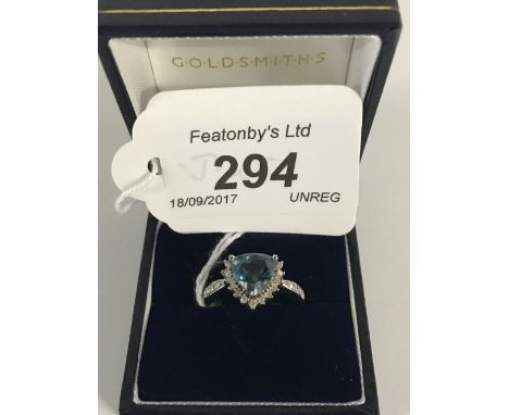 9CT WHITE GOLD RING WITH TRIANGULAR CUT TOPAZ SURROUNDED BY DIAMONDS.