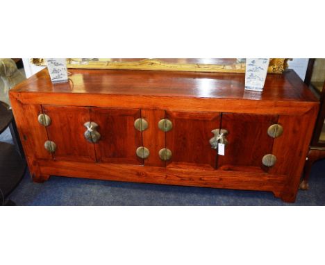 A Chinese hardwood low cabinet, of rectangular form, the four doors with brass escutcheons and hinges, raised on bracket feet